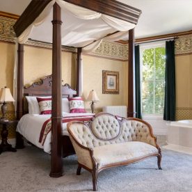 Large spacious room with carpet floor and a four poster queen bed with a jetted tub